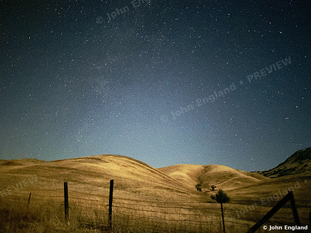 Milky Way Over Golden Hills – Milky Way core rising over golden grass hills and a ranch fence.