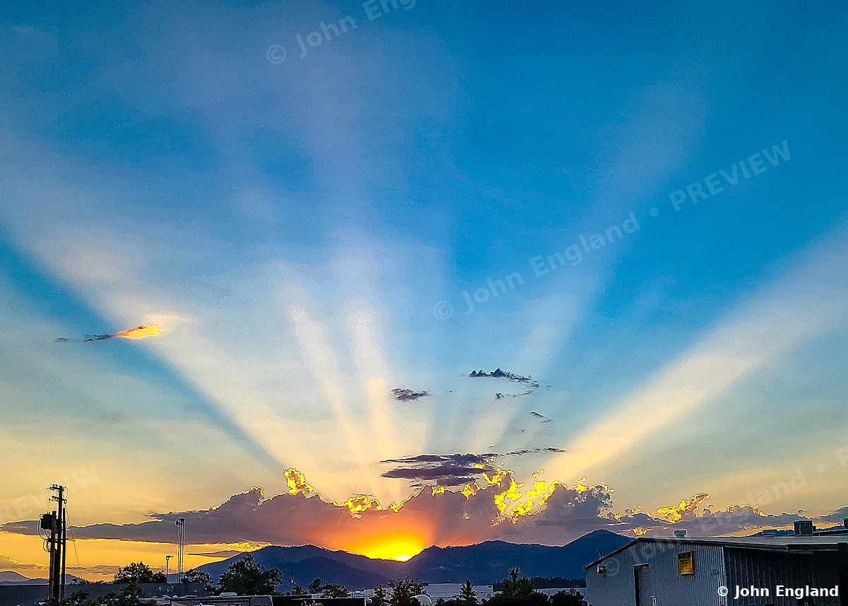 Sunbeams over the Hills – Crepuscular rays fanning from a setting sun over distant hills.