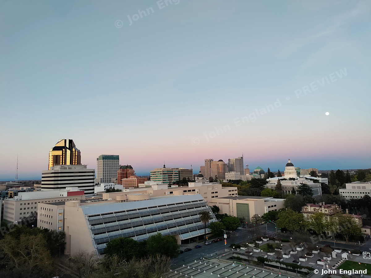 Downtown Sacramento Rooftops at Dusk with Moon – Elevated dusk view over downtown Sacramento rooftops with the moon in a pastel sky, CA. Mar 27, 2021. John England.