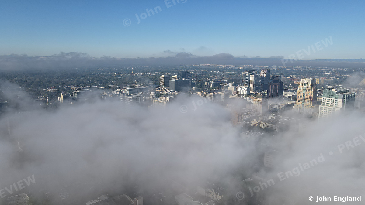 Sea of Fog over Downtown Sacramento – Morning fog rolls over Sacramento like an ocean, with only the tallest downtown towers breaking through under a clear blue sky. Aerial photograph © John England.