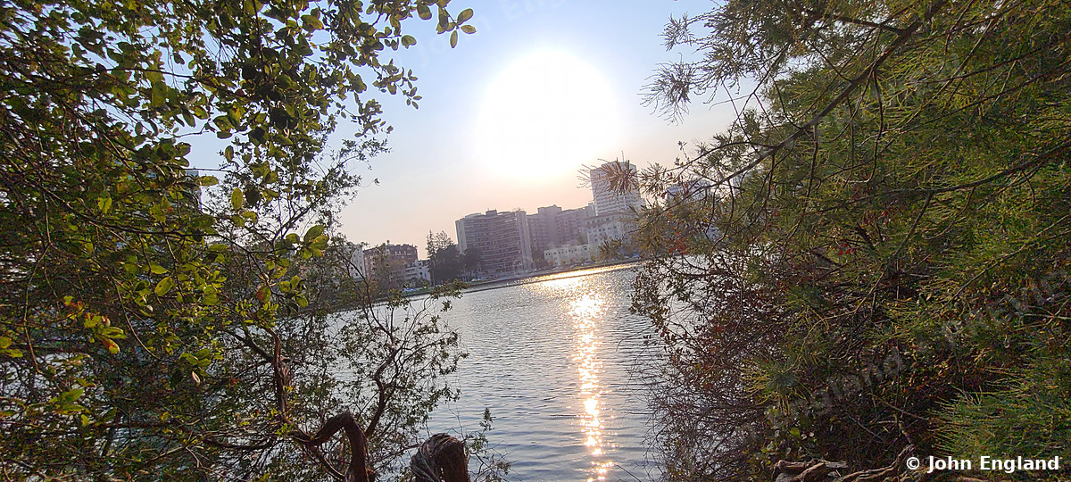 Riverside Sunburst – Sun over a river with distant city towers, Aug 28, 2020.