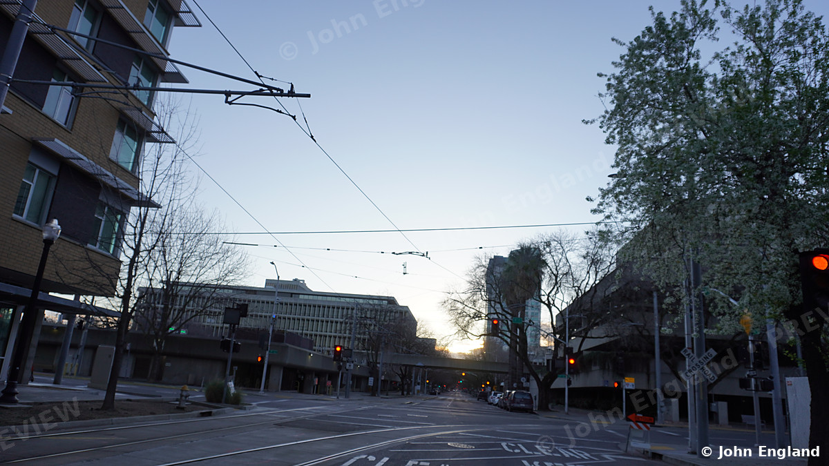 Sunrise Down a Sacramento Street – Sunrise down a tree-lined downtown Sacramento street with light-rail wires, CA. Feb 2021. John England.