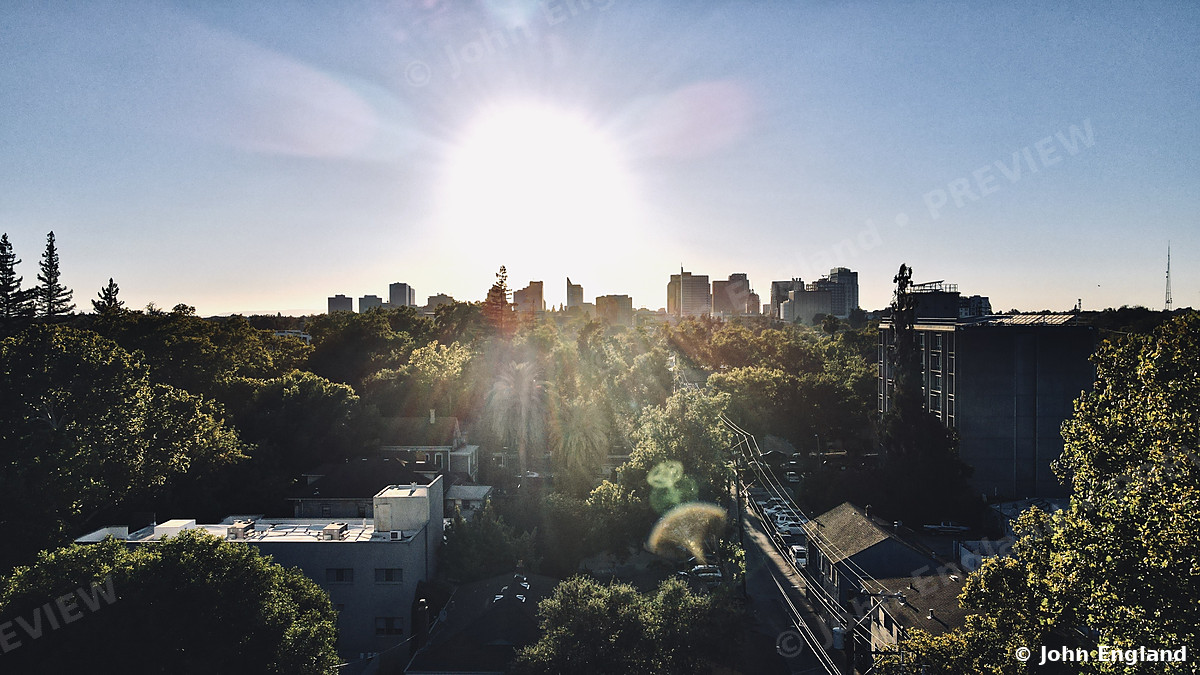 Sun Over the Sacramento Skyline – Drone view of the sun setting over tree-lined Midtown toward the downtown Sacramento skyline. Aug 9, 2022. John England.
