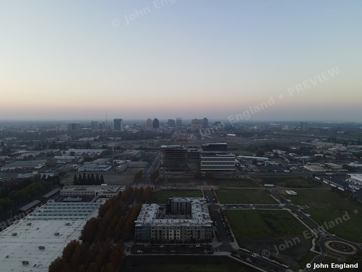 City at Dusk from Above – Drone view across the city toward a downtown skyline at dusk. John England.