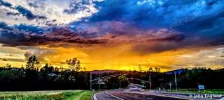 Storm Sunset over the Road – Dramatic storm clouds and orange sunset over a roadside tree line.