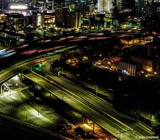 Interchange Glow – Aerial night of curving freeway light trails.