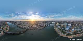 360° Planet Panorama Over the River at Sunset – 360° drone panorama over a river and downtown at sunset. John England.